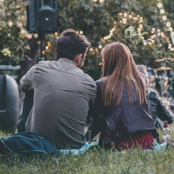 Ein Mann und eine Frau sitzen auf einer Wiese mit Blick auf eine beleuchtete Außenkulisse